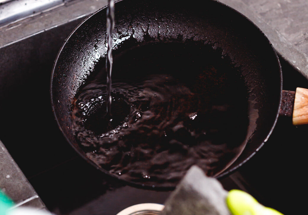 Das Bild zeigt wie eine fettige Pfanne in der Spüle gesäubert wird